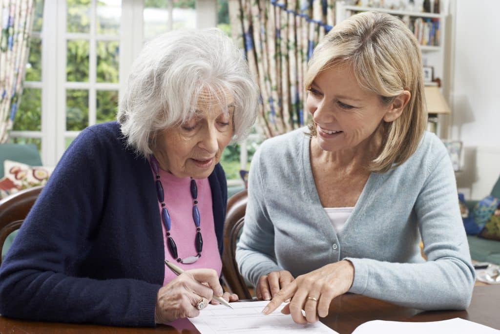 A neighbor helping a senior woman write out a will.